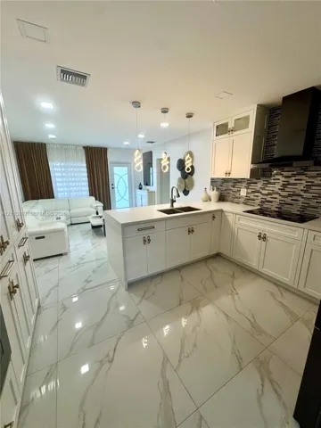 Kitchen featuring white cabinetry, solid-surface countertops, a tiled backsplash, large-format veined flooring, and three pendant light fixtures
