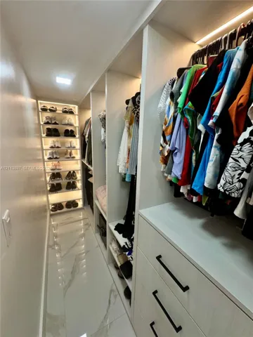 Custom walk-in closet featuring floor-to-ceiling built-in shelving, integrated LED accent lighting, three-drawer cabinetry with matte black hardware, and large-format porcelain tile flooring