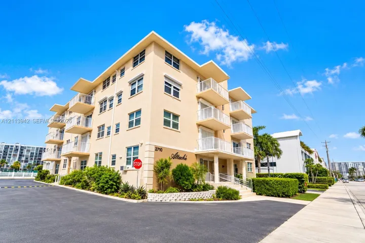 Multi-story building exterior featuring smooth stucco finish, tiered private balconies with metal railings, and integrated ground-level landscaping