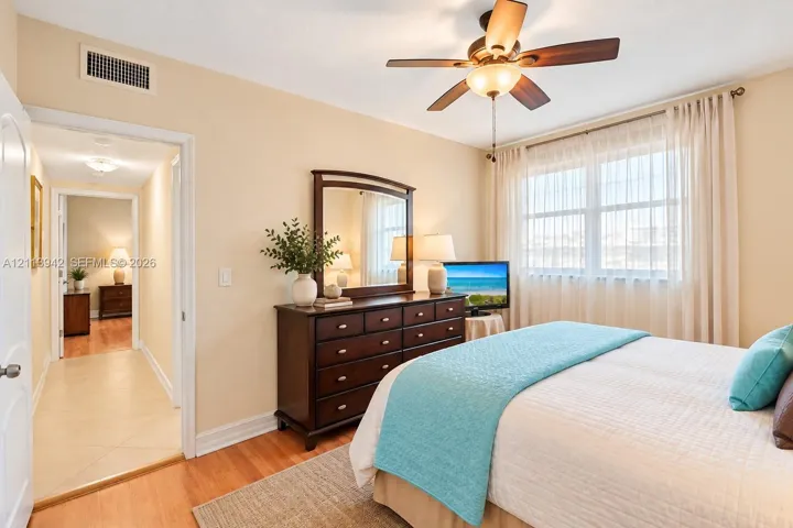 Room featuring wood-finish flooring, a multi-blade ceiling fan with integrated lighting, and a large window with horizontal blinds