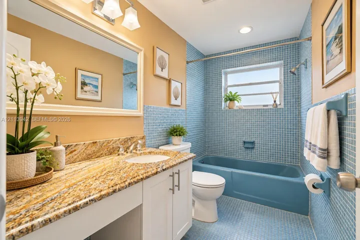 Bathroom featuring a white vanity with stone-top surfacing, integrated porcelain sink, blue mosaic tile walls, and a matching blue porcelain bathtub