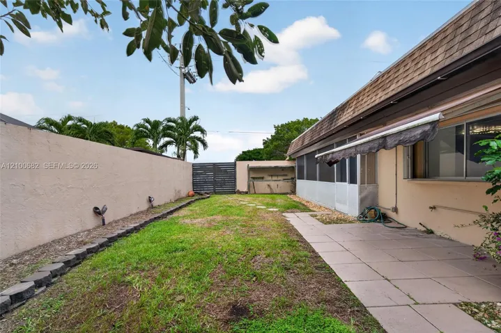 Back yard featuring a concrete paver patio, screened-in enclosed patio, perimeter privacy wall, and newer horizontal slat gate*