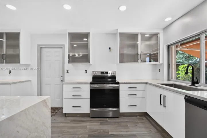 Kitchen featuring white cabinetry with glass-front uppers, solid surface countertops, stainless steel appliances, recessed lighting, and vinyl wood-finish flooring