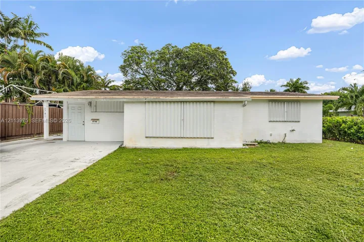 Single-story exterior featuring a light-toned facade, flat roofline, concrete driveway, and attached metal storm shutters