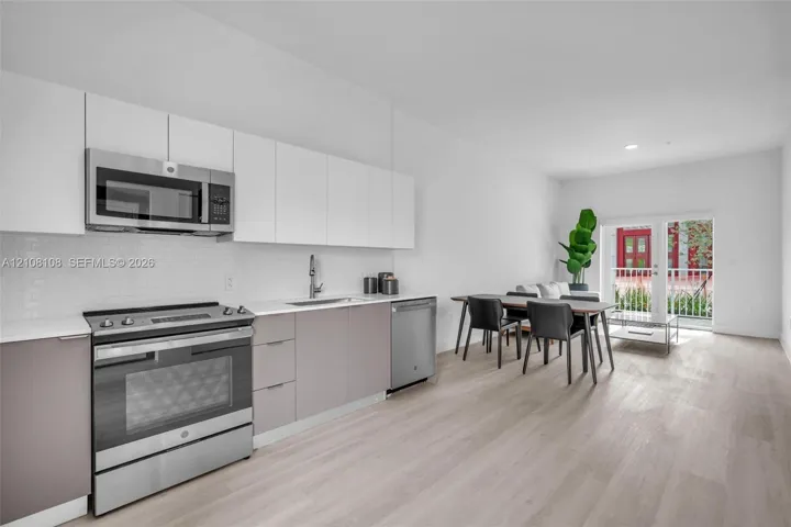 Kitchen featuring two-tone flat-panel cabinetry, stainless steel appliances, white subway tile backsplash, quartz countertops, and wood-finish flooring