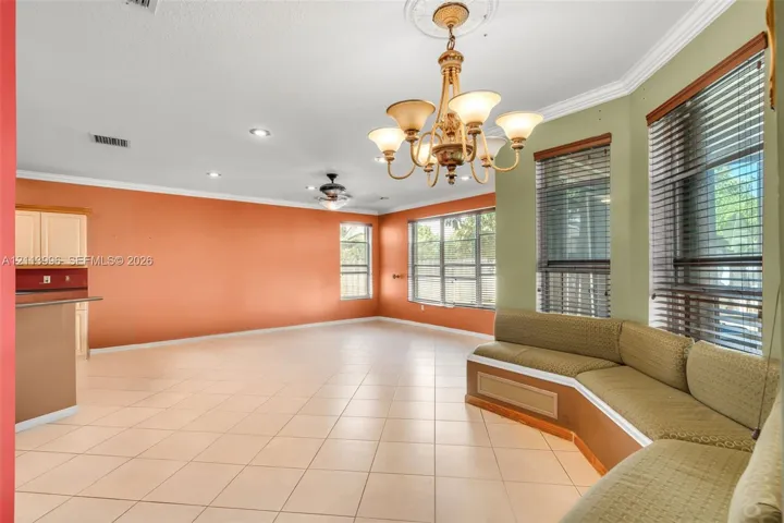 Open-concept room featuring tile flooring, crown molding, a decorative ceiling medallion with an attached multi-arm chandelier, and a custom built-in bench