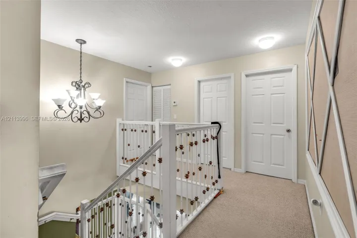 Traditional-style chandelier with scrolling metal arms, white six-panel interior doors, and railing featuring vertical balusters with decorative detailing