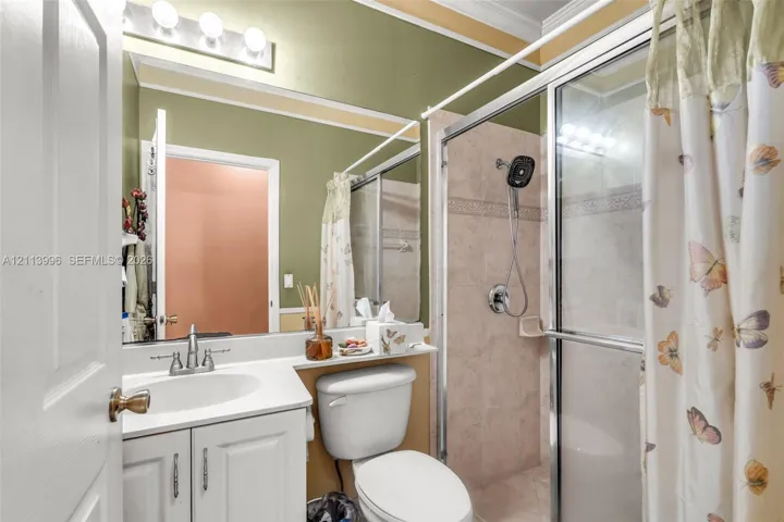 Bathroom featuring a white vanity with an integrated sink, polished chrome faucet, large vanity mirror with overhead lighting, and a glass-enclosed shower with tile surround