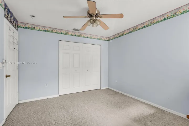 Room featuring neutral carpeting, a ceiling-mounted fan with integrated lighting, and a double-panel closet with white doors