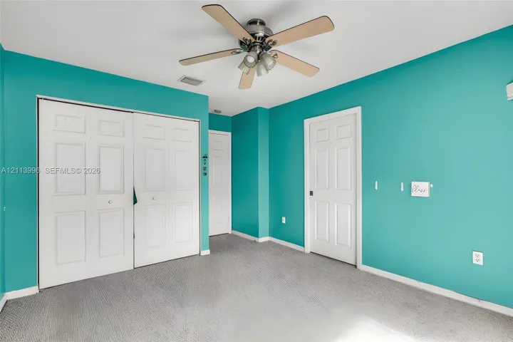 Room featuring gray carpeting, a multi-blade ceiling fan with integrated light fixture, and double-panel closet doors