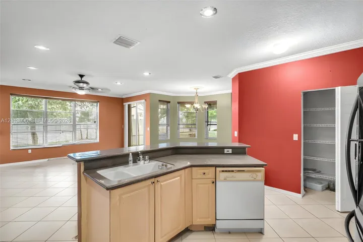 Kitchen island featuring a dual-basin sink, neutral-toned cabinetry, solid surface countertop, built-in dishwasher, and a walk-in pantry
