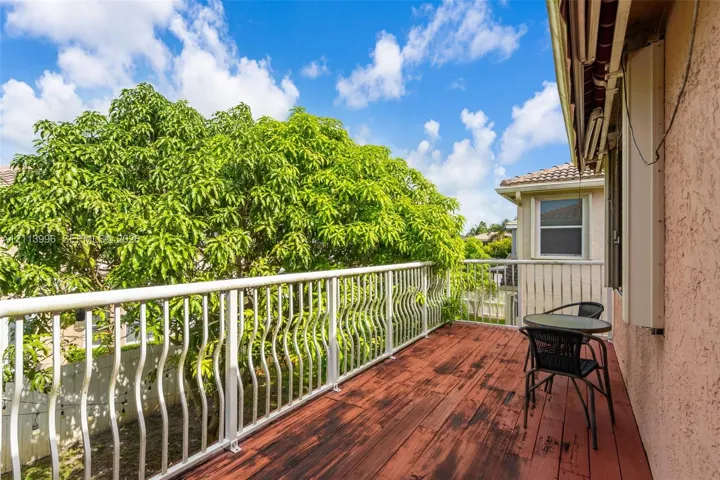 Exterior balcony featuring wood-finish decking, white metal railing, and stucco wall siding