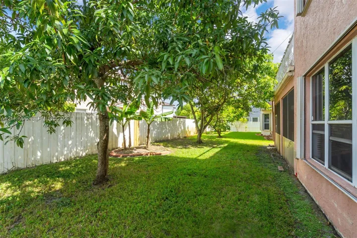 Backyard featuring mature trees, a manicured lawn, a white privacy fence, and an exterior screen enclosure