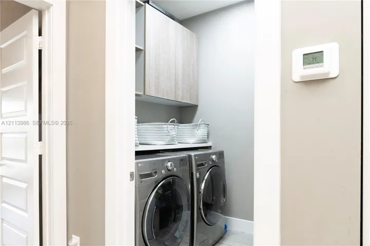 Laundry closet featuring custom wood-finish cabinetry, solid surface shelving, and a wall-mounted digital climate control thermostat