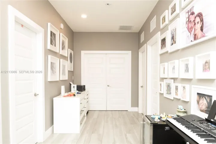 Hallway featuring light-toned wood-finish flooring, neutral wall paint, recessed lighting, and multiple white multi-panel doors