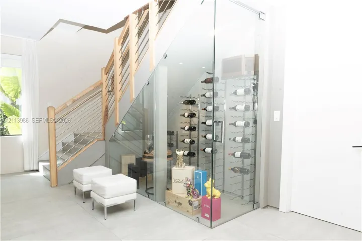 Glass-enclosed wine storage with metal racking, featuring a staircase with wood handrails and horizontal metal cable railing