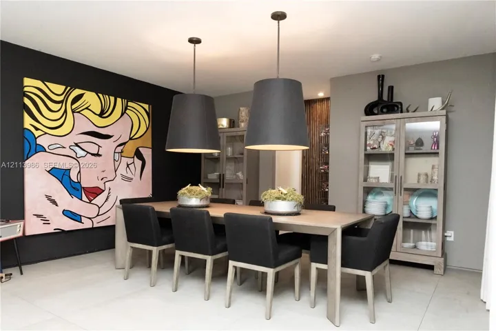 Large-format dining area featuring two suspended black pendant lights, light-toned stone-finish flooring, and a vertical wood-slat accent wall