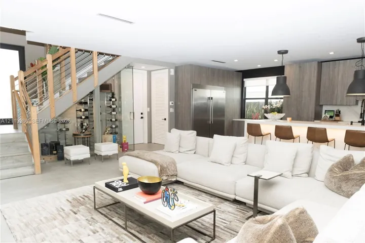 Open-concept kitchen featuring flat-panel cabinetry and stainless steel appliances, glass-enclosed wine storage, and a cable-railing staircase with wood handrails