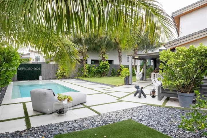 Outdoor living space featuring an in-ground swimming pool, large format concrete pavers with artificial turf inlay, covered patio area, and perimeter landscaping