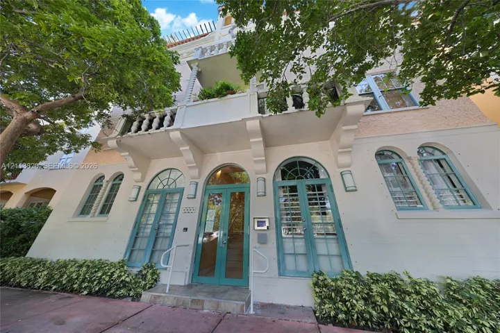 Mediterranean-inspired exterior featuring stucco facade, arched multi-pane glass entry doors, second-story balcony with decorative balustrade, and symmetrical arched window detailing