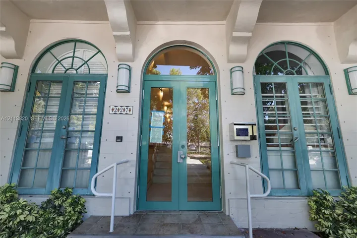 Entrance featuring arched glass-paneled double doors, flanking arched windows with teal frames, decorative corbel accents, and wall-mounted exterior sconces