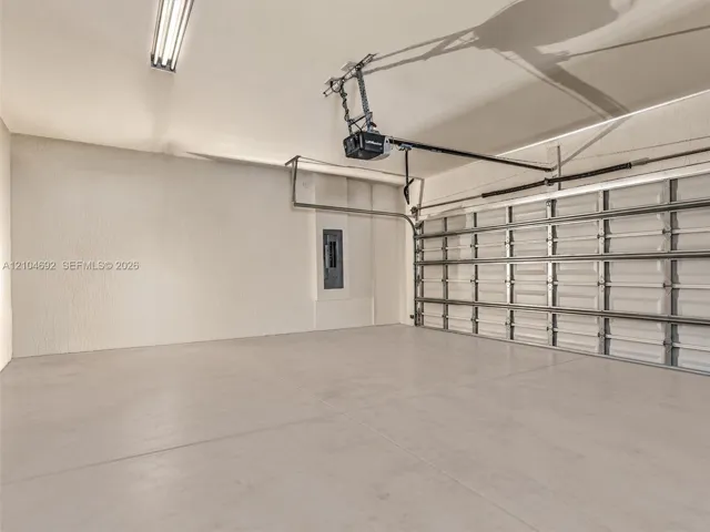 Finished garage interior featuring concrete flooring, textured walls, a multi-panel overhead door, and an integrated electrical service panel