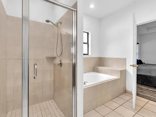 Shower enclosure featuring a glass door, neutral-toned wall tiles, a built-in recessed shelf, and a detachable showerhead, paired with a built-in soaking tub surrounded by matching tile finish