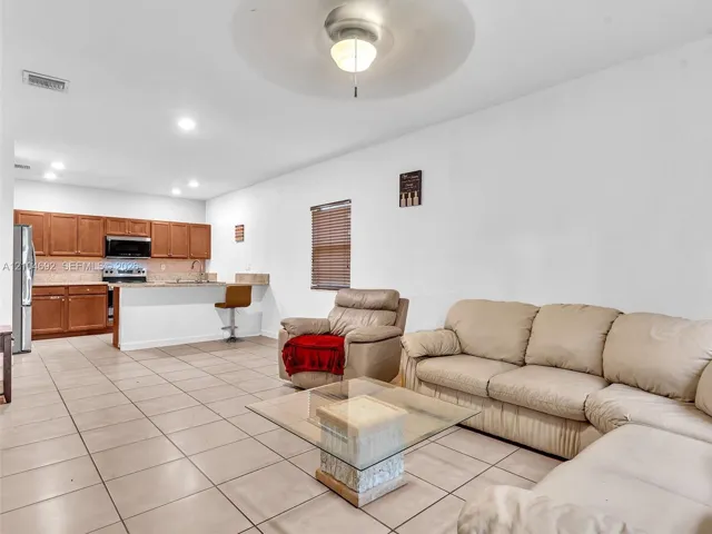 Open-concept interior featuring large-format tile flooring, wood cabinetry, stone countertops, a breakfast bar, and recessed lighting