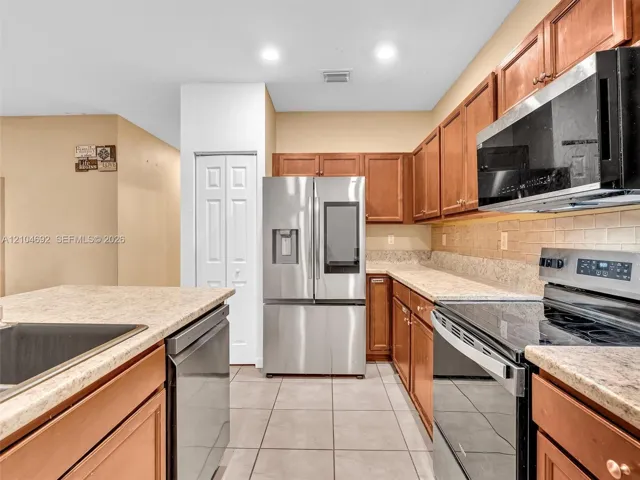 Kitchen featuring warm-toned wood cabinetry, neutral countertops, tile flooring, and integrated stainless steel appliances