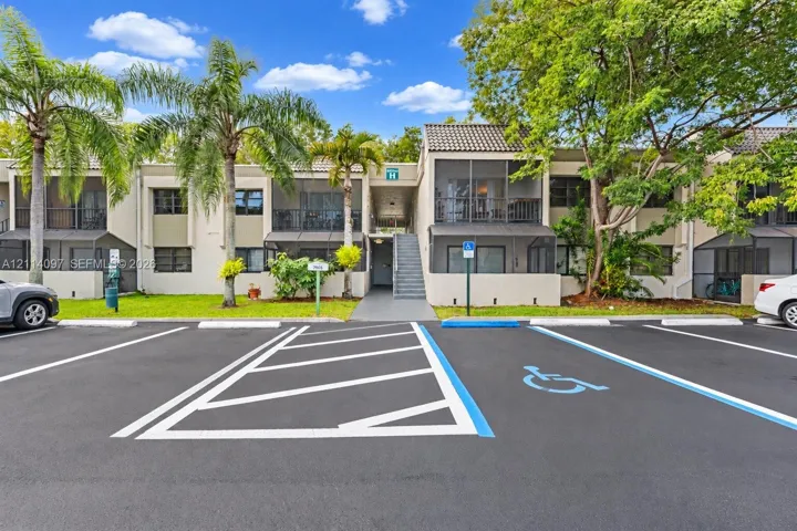 Two-story exterior featuring a neutral stucco facade, tile roofing, screened-in balconies, and mature landscaping