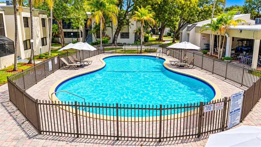 Community swimming pool featuring a paved deck, perimeter metal fencing, and surrounding mature palm trees