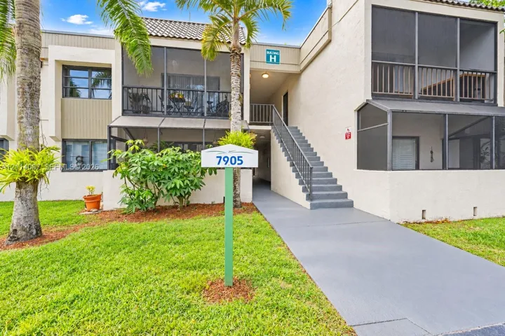 Multi-level stucco exterior featuring screened balconies, covered staircase with metal railing, and paved entry walkway