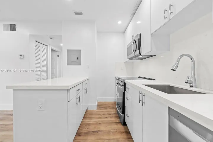 Kitchen featuring high-gloss white cabinetry, quartz countertops, a stainless steel under-mount sink with a gooseneck faucet, stainless steel appliances, and wood-finish flooring