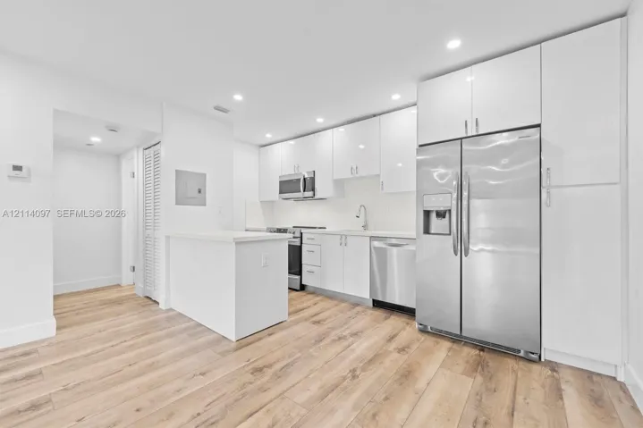 Kitchen featuring white high-gloss cabinetry, stainless steel appliances, wood-finish flooring, quartz countertops, and recessed lighting