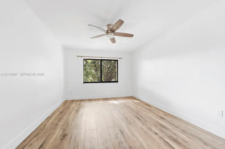 Neutral interior featuring wood-finish flooring, a ceiling fan with integrated lighting, and a window with a dark frame