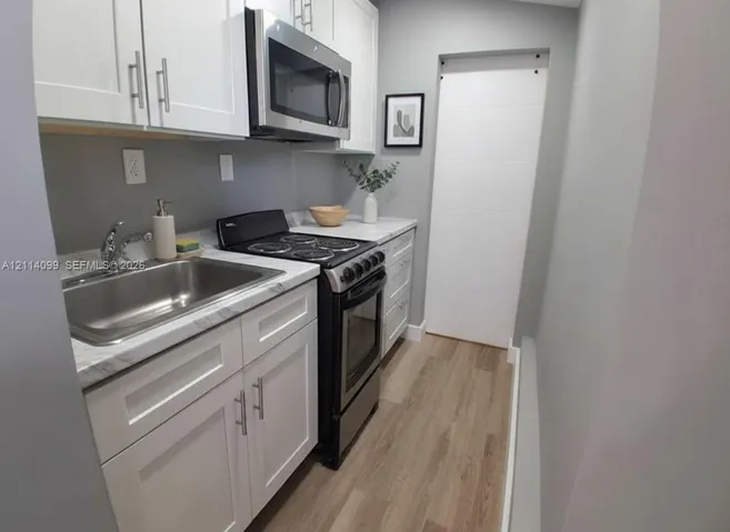 Kitchen featuring white shaker-style cabinetry, stone-finish countertops, stainless steel appliances, a stainless steel sink, and wood-finish flooring
