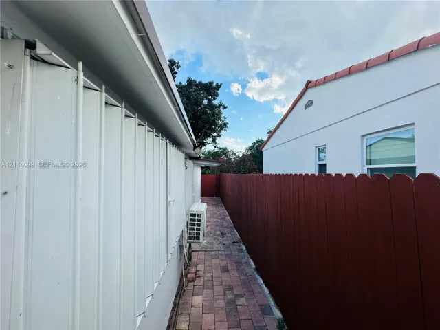 Exterior side walkway featuring brick paver flooring, vertical siding, and a wood privacy fence