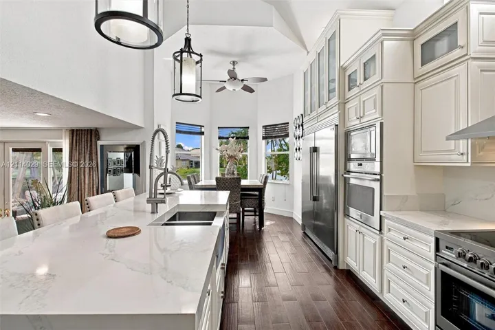 Kitchen featuring a quartz-topped island with an undermount sink, custom cabinetry with glass-front uppers, stainless steel built-in appliances, wood-finish flooring, and vaulted ceilings