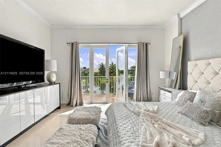 Double glass-paned doors opening to a private balcony, polished tile flooring, crisp crown molding, and built-in glossy white cabinetry