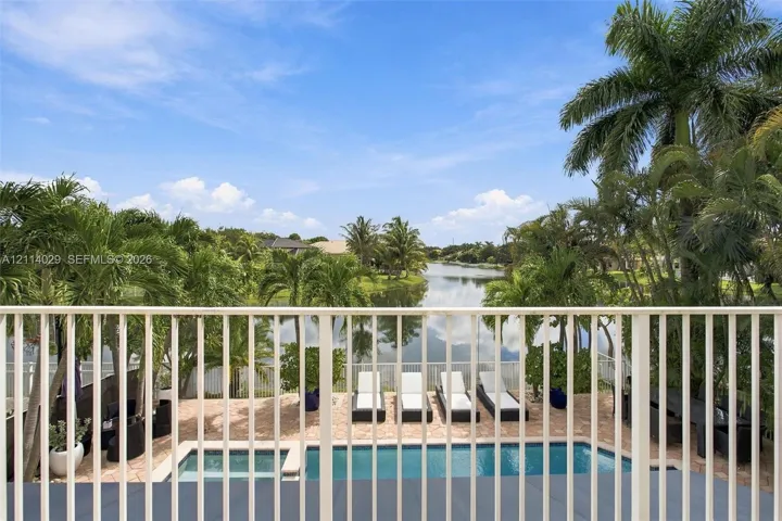 Outdoor patio featuring a swimming pool, integrated spa, stone-paver decking, and metal balcony railing with water frontage