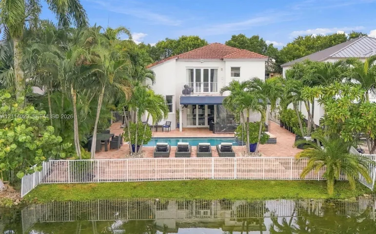 Waterfront rear exterior featuring a swimming pool, expansive brick-paver patio, second-story balcony, and mature tropical landscaping