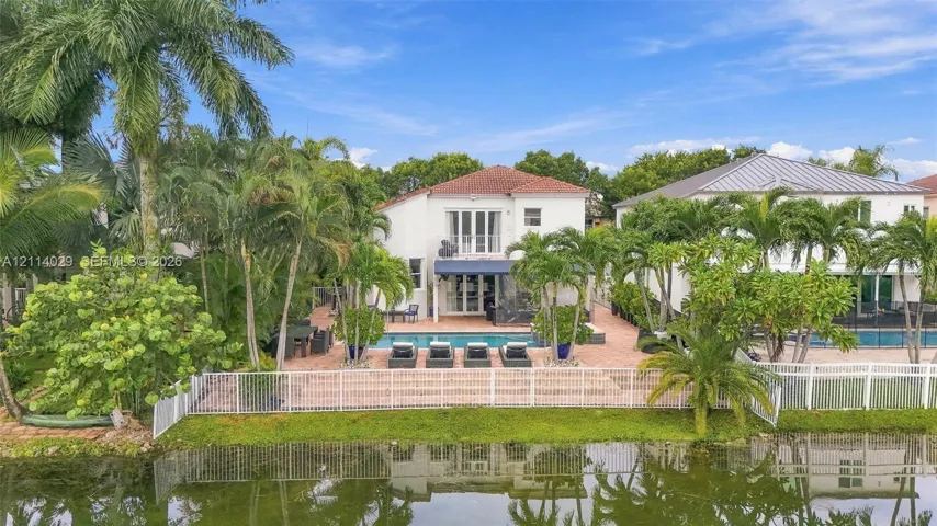 Waterfront residence featuring a swimming pool, paved patio, balcony with glass railing, and mature palm landscaping