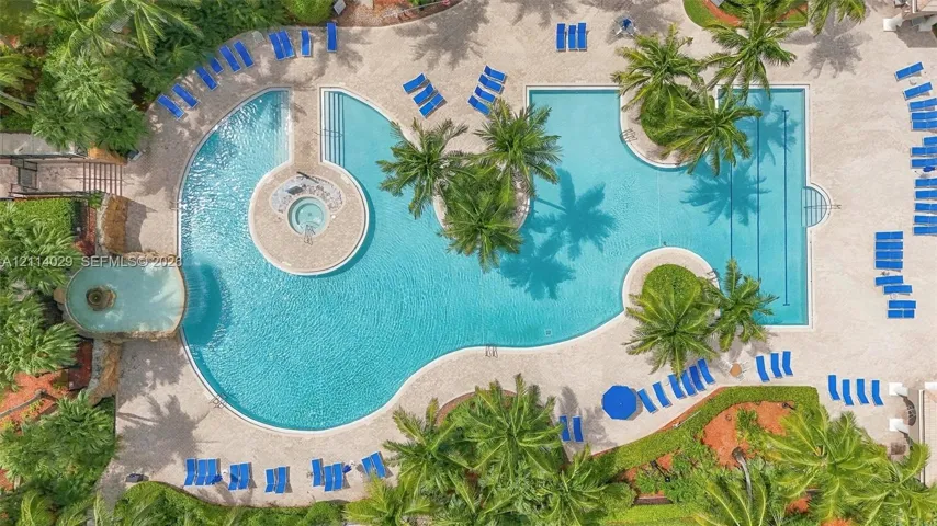 Expansive swimming pool featuring an integrated spa, a stone-accented water feature, palm landscaping, and stone-paver decking