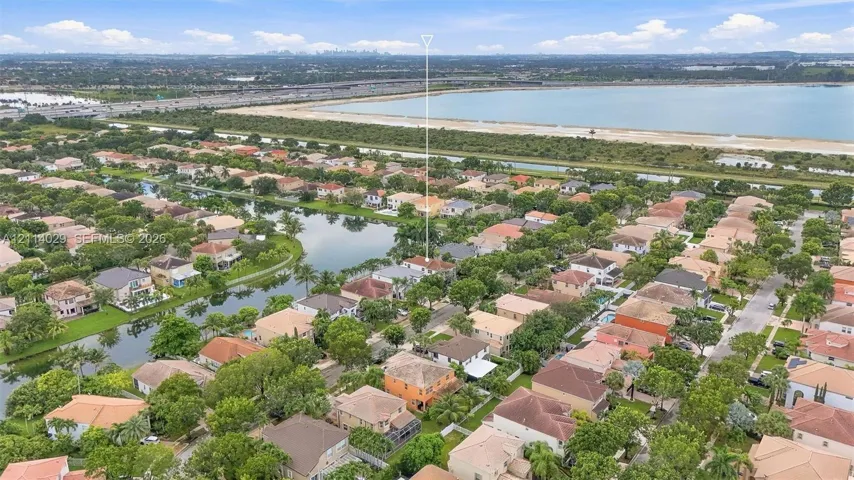 Aerial perspective of a residential property situated in a planned community featuring a lake, tree-lined streets, and proximity to a large body of water