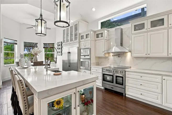 Kitchen featuring white cabinetry with glass-front uppers, solid surface countertops, a professional-grade stainless steel range with matching vent hood, and wood-finish flooring