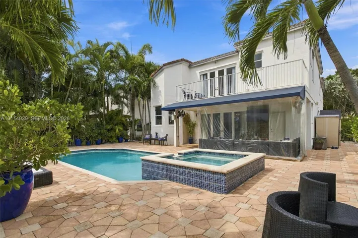 Exterior features including a swimming pool with a raised tiled spa, expansive paver patio, second-story balcony with metal railing, and retractable exterior awning