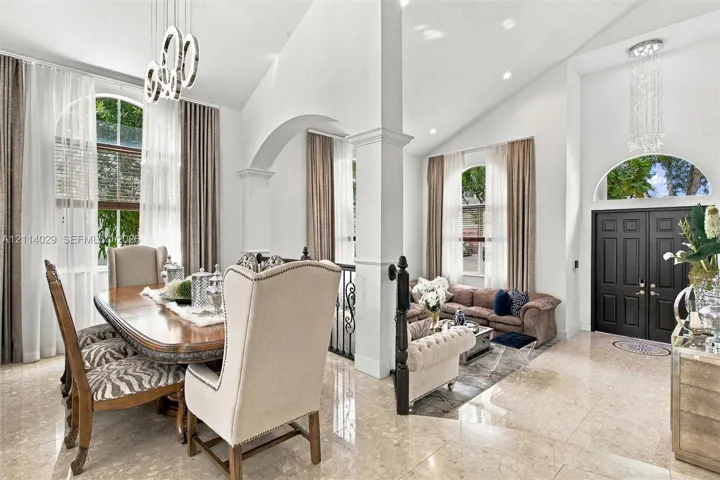 Vaulted ceilings, expansive stone flooring, arched architectural detailing, modern circular pendant lighting, and a double-entry front door with a half-moon transom window