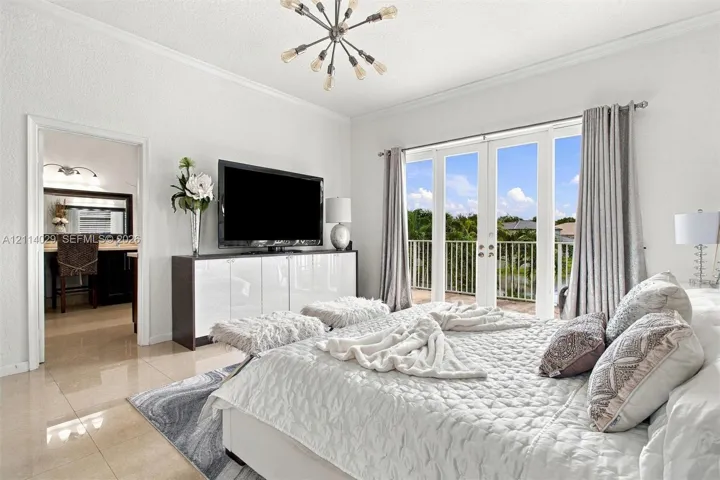 Polished tile flooring, modern sputnik-style chandelier, and double French doors opening to a railed balcony
