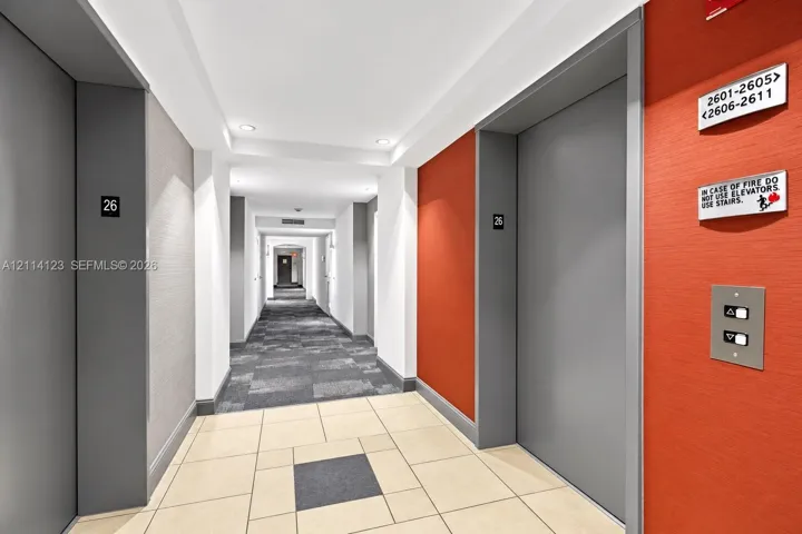 Elevator lobby featuring metallic-finish doors, textured wall treatments, integrated recessed lighting, and large-format ceramic tile flooring