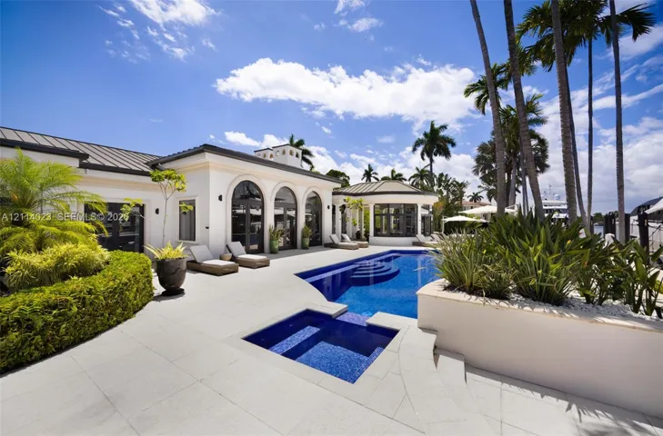 Outdoor living area featuring a tile-surround pool and spa, arched architectural openings, manicured landscaping, and a metal roof